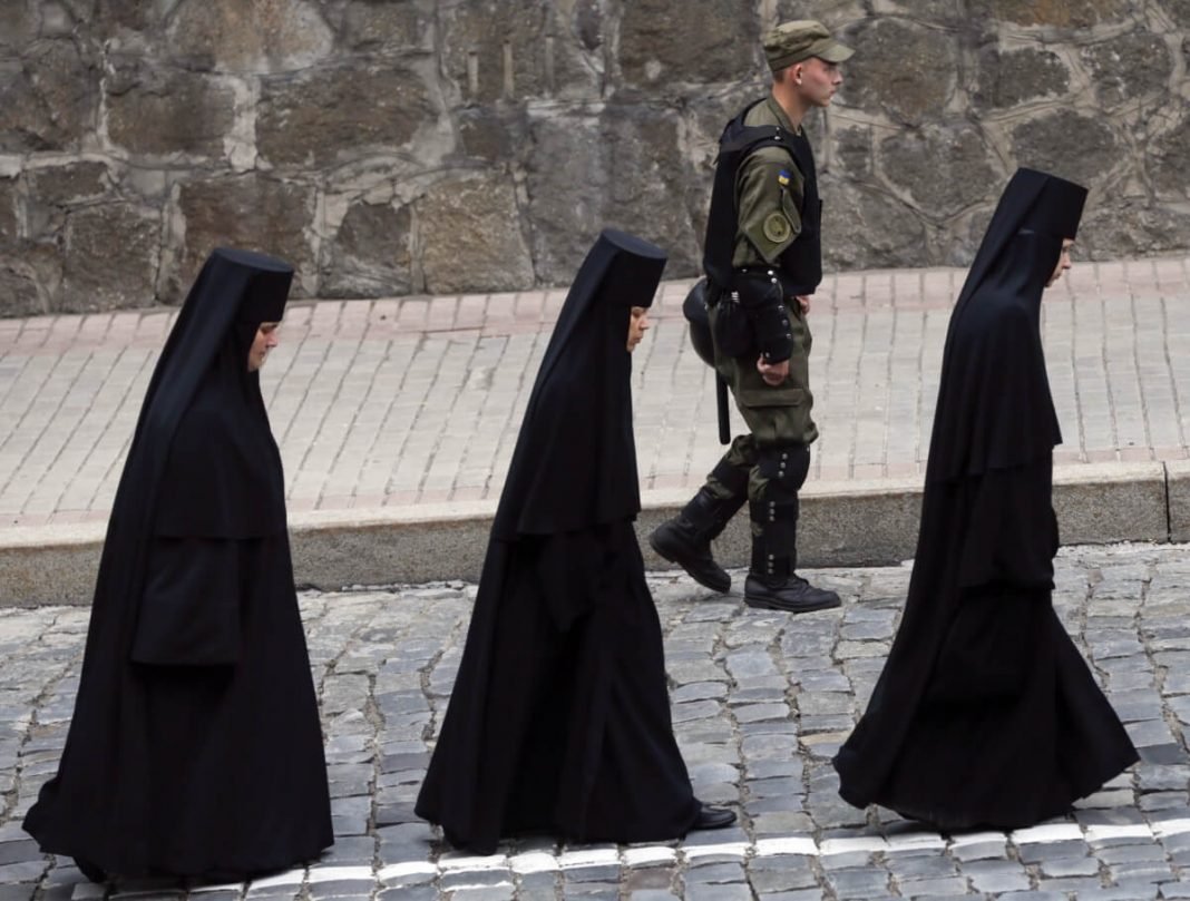 Irmãs ortodoxas caminham ao lado de um policial na Ucrânia