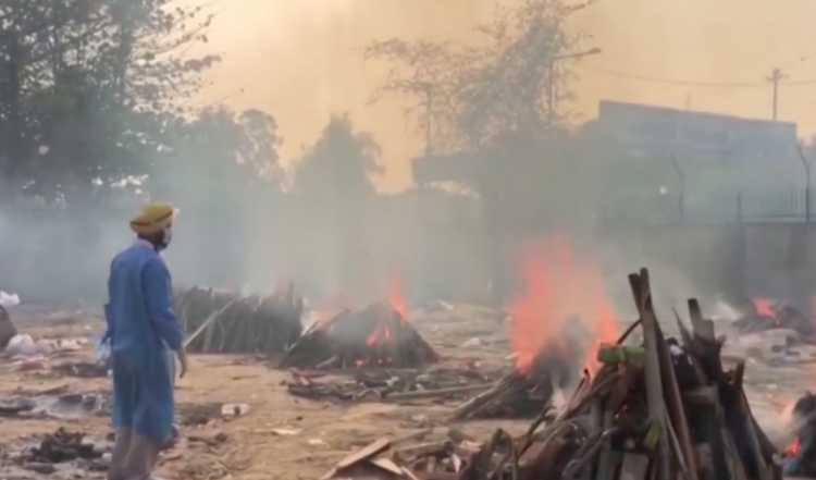 Um profissional de saúde supervisiona cremações ao ar livre em Delhi.