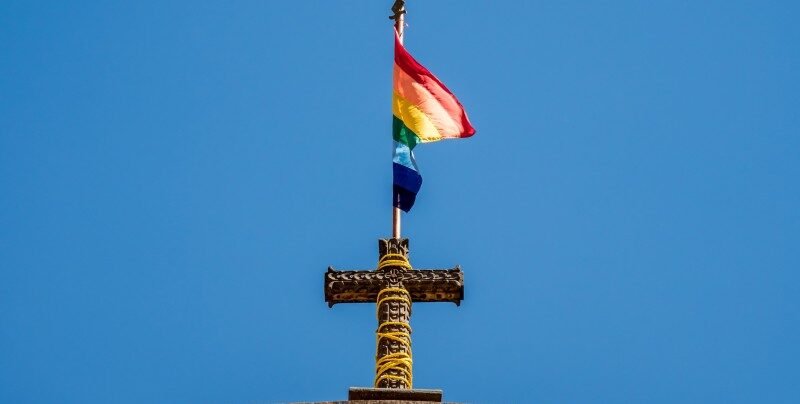 Bandeira LGBT sobre uma cruz no topo de uma igreja