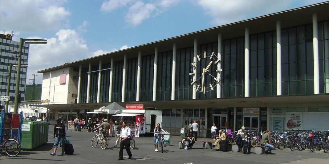 Cena de crime em estação de trem alemã com fita policial e investigadores.