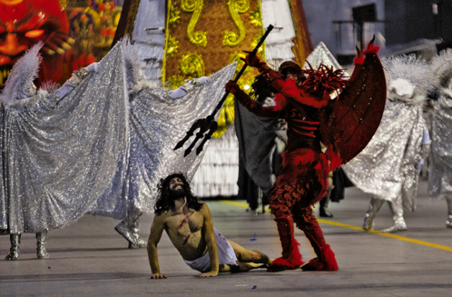 Foliões em um bloco de Carnaval com foco em uma fantasia com símbolo religioso estilizado.