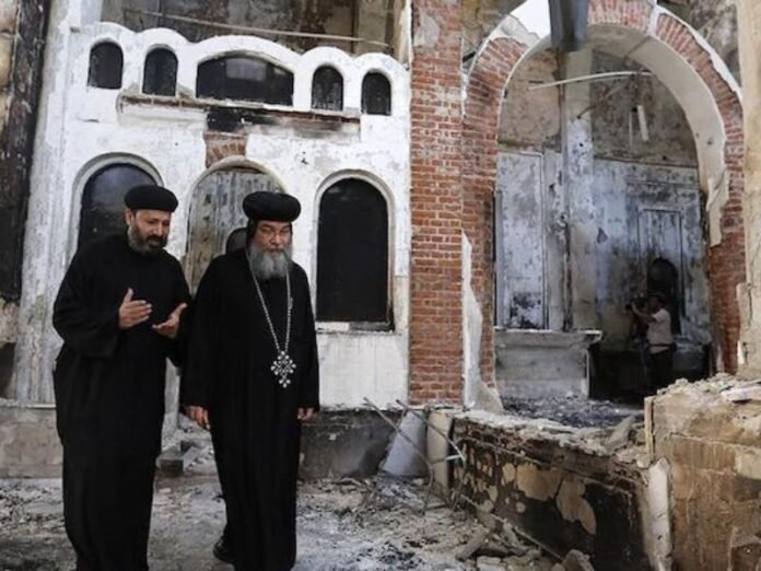Rua de vilarejo egípcio com tensão após ataque de multidão, mostrando sinais de vandalismo e observadores apreensivos.