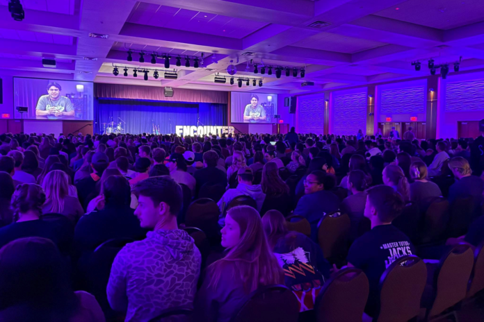 Jovens participam de evento de avivamento em universidade americana Jovens estudantes em um evento religioso lotado em uma universidade americana, com expressões de fervor e atenção.