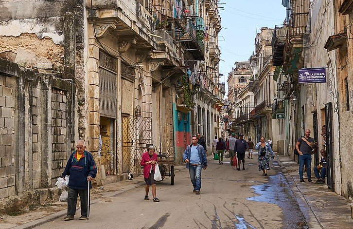 Criança cubana revirando lixo em busca de comida em rua suja e desolada.
