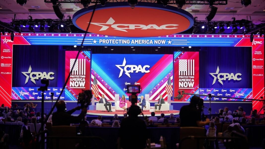 Participantes da CPAC 2026 discutindo política em um salão de conferências.