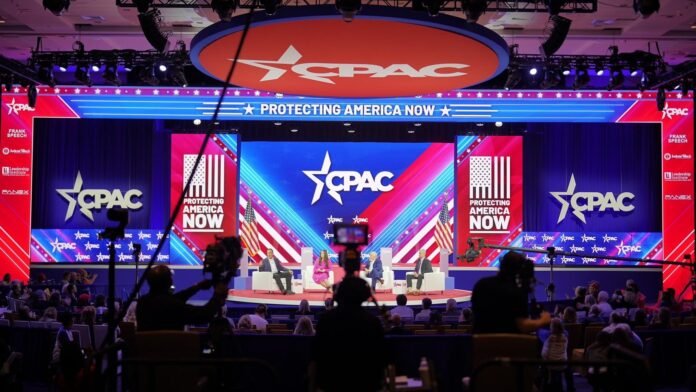Participantes da CPAC 2026 discutindo política em um salão de conferências.