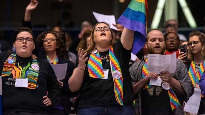 Manifestantes exibem cartazes de apoio a direitos transgêneros em frente a um prédio institucional.