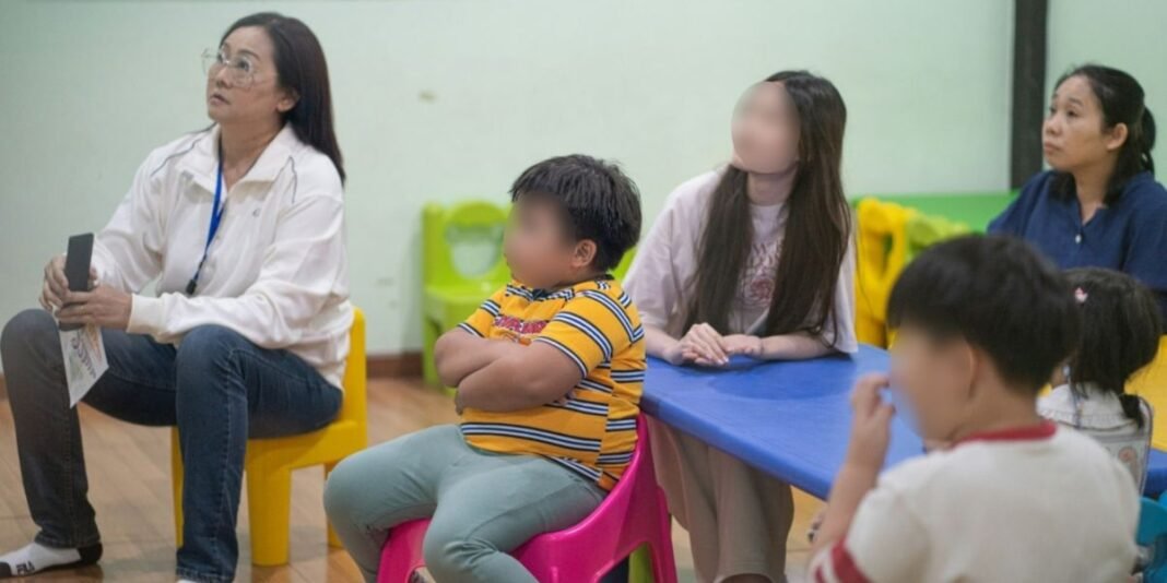 Crianças asiáticas participando de aula de reforço escolar em um centro comunitário com a supervisão de um missionário.