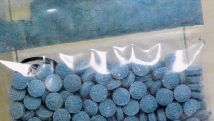 Close-up de pílulas coloridas, algumas parecendo medicamentos prescritos, sobre fundo escuro.