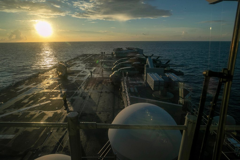 Navio de guerra USS Tripoli navega em águas do Golfo Pérsico com a Ilha Kharg ao fundo.