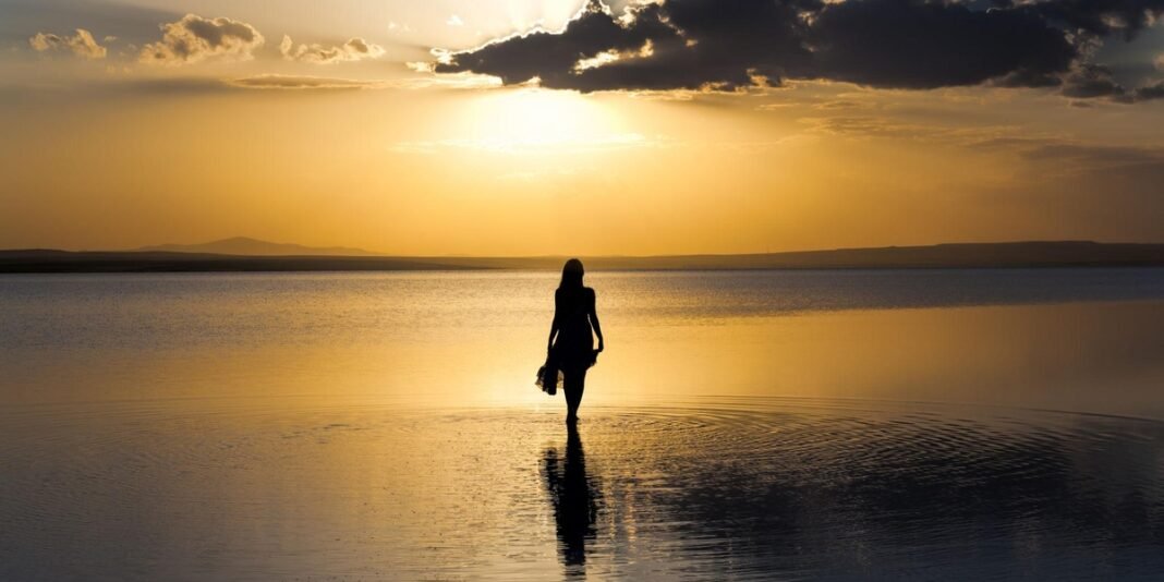 Mulher respirando profundamente em um parque ao amanhecer, simbolizando autocuidado e serenidade.