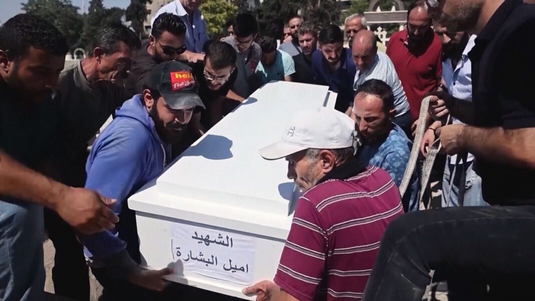 Igreja cristã em ruínas após um ataque, com fumaça ao fundo.