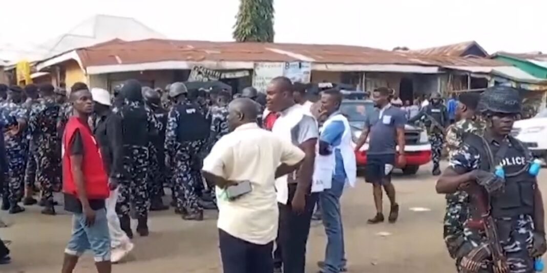 Vila nigeriana destruída após ataque terrorista, com sobreviventes observando a devastação.