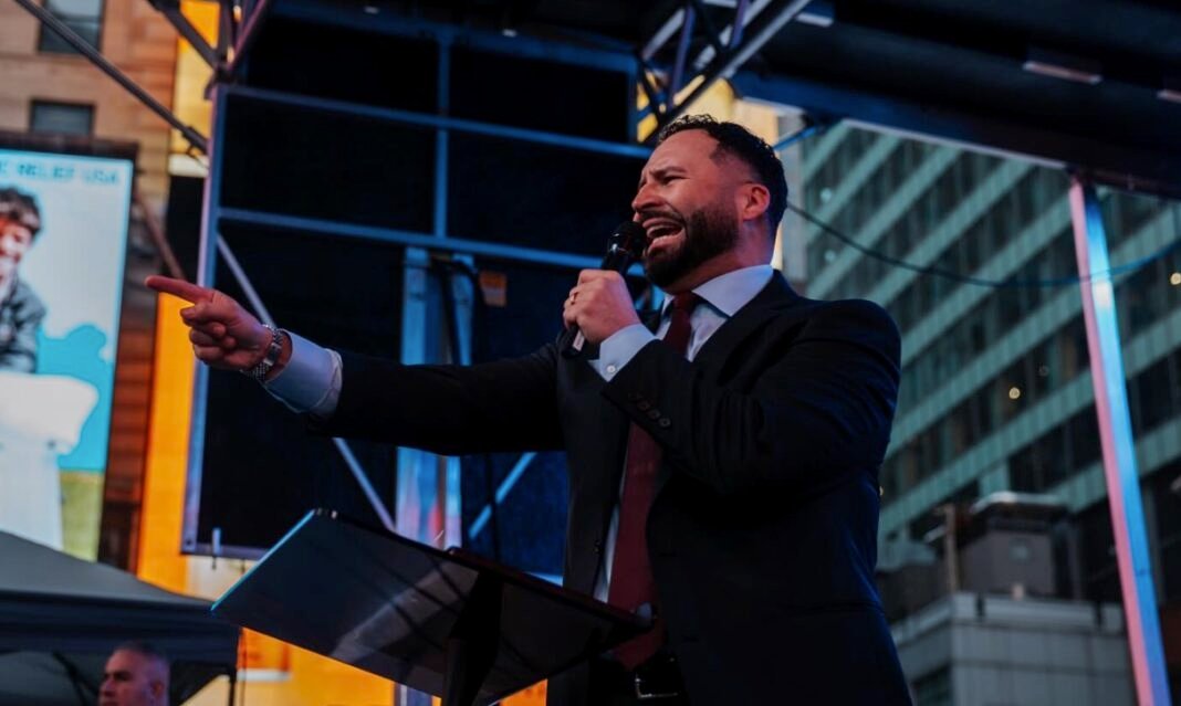 Multidão em um culto religioso na Times Square, Nova York, com o pastor no púlpito e pessoas demonstrando fortes emoções.