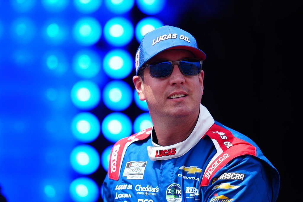 Kyle Busch celebrando vitória no pódio da NASCAR com troféu.