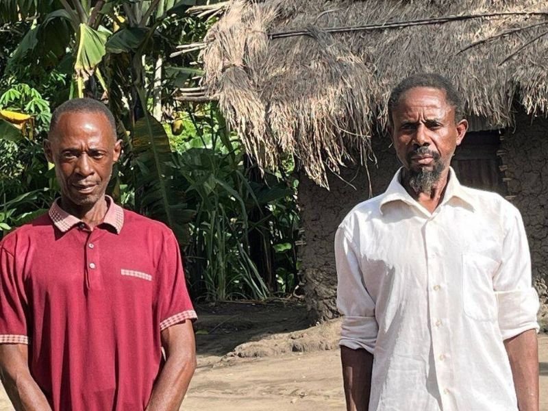 Dois homens ugandenses libertados da prisão sorriem aliviados em frente a uma igreja