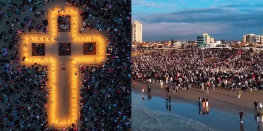 Multidão reunida na orla de Balneário Rincão para culto ao amanhecer com cruz iluminada ao nascer do sol.