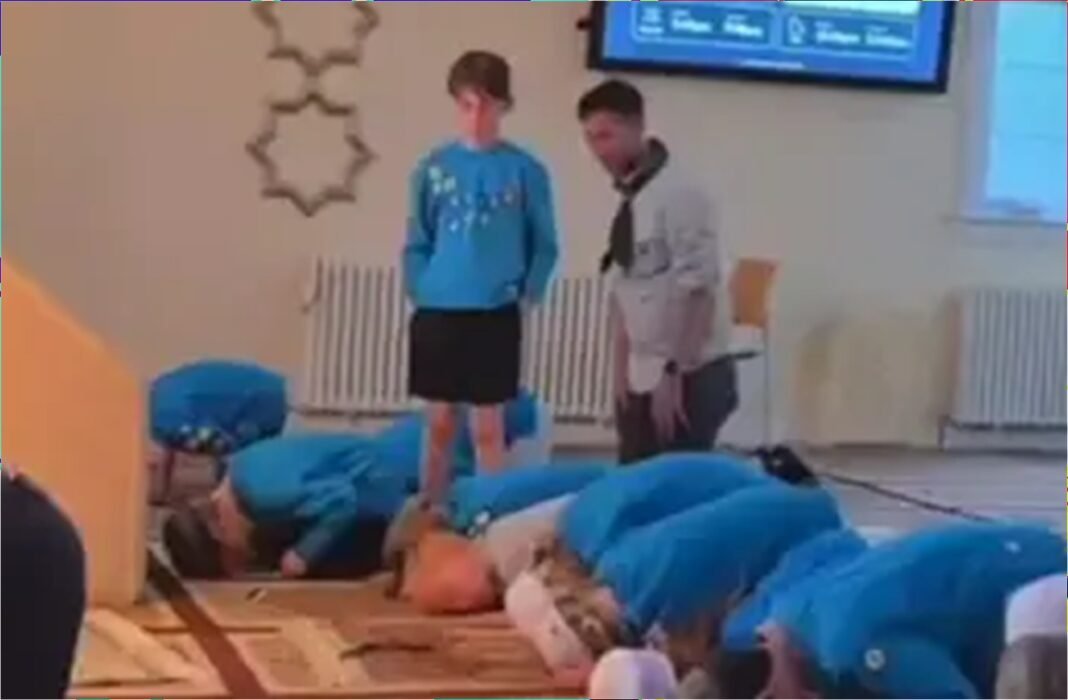 Jovem em pé durante ritual muçulmano enquanto outros se ajoelham.