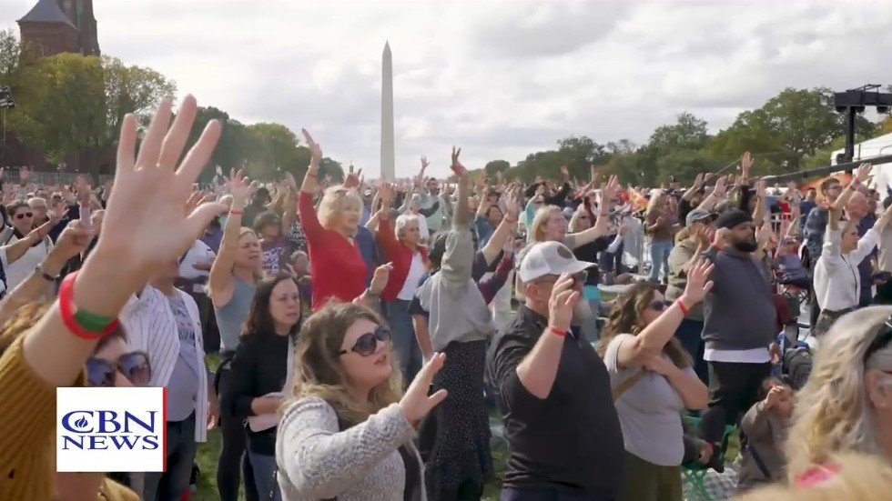 Multidão reunida no National Mall para o evento 'Rededicate 250' com o Monumento a Washington ao fundo.