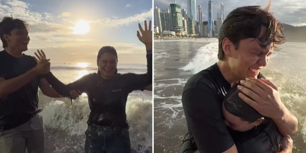 Líder batiza irmã caçula em praia de Santa Catarina, com multidão assistindo.