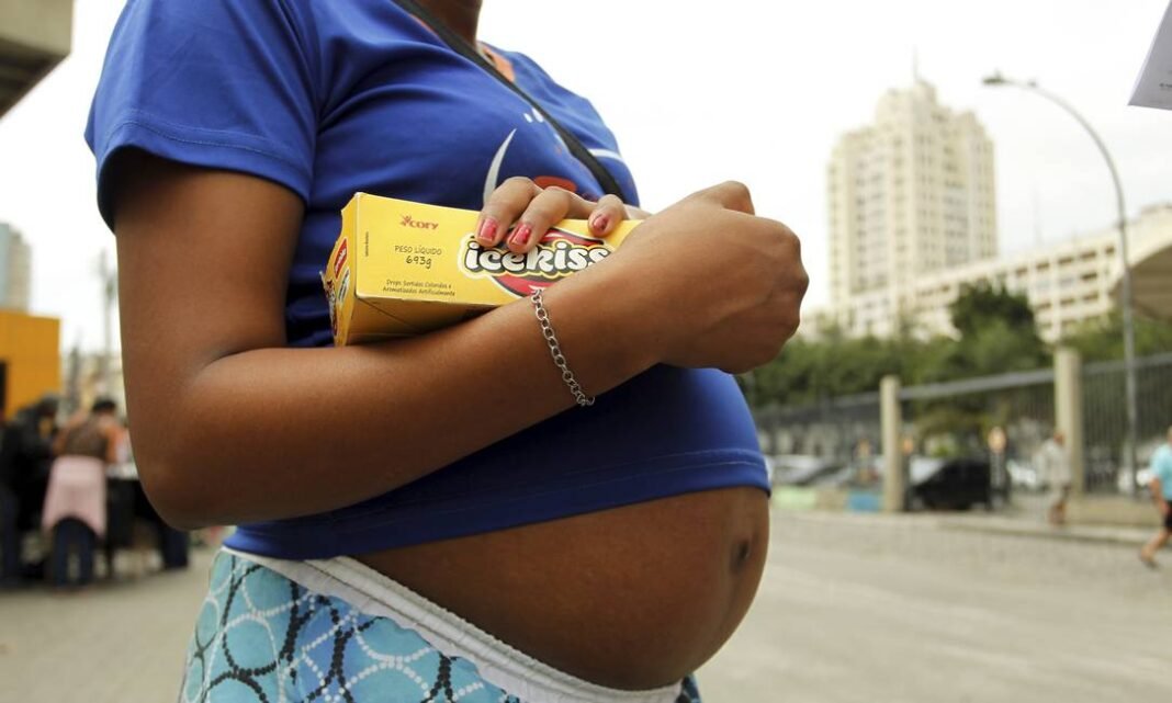 Jovem mãe sorri para seu bebê no colo em um parque, simbolizando esperança e apoio recebido.