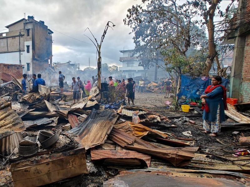 Estrada dividida por barricada em Manipur, com presença de segurança governamental e casas danificadas.