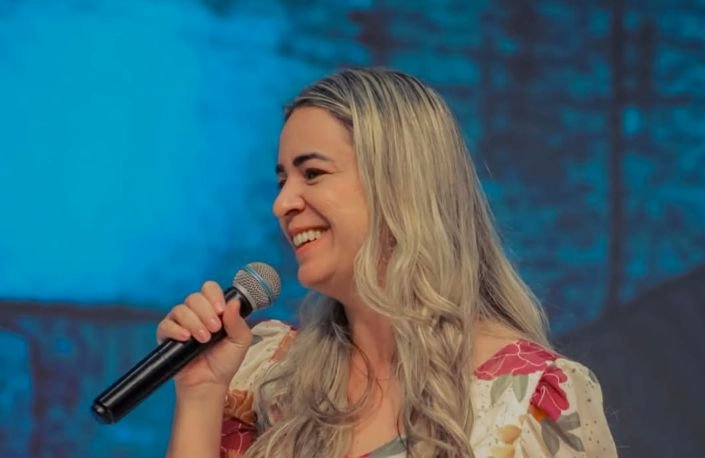 Missionária Keyla Costa em pé, sorrindo e ministrando em um evento