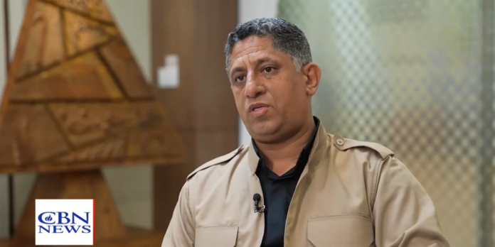 Pastor compartilha jornada de fé após visão em prisão Pastor Nihad compartilhando seu testemunho em uma sala de espera.