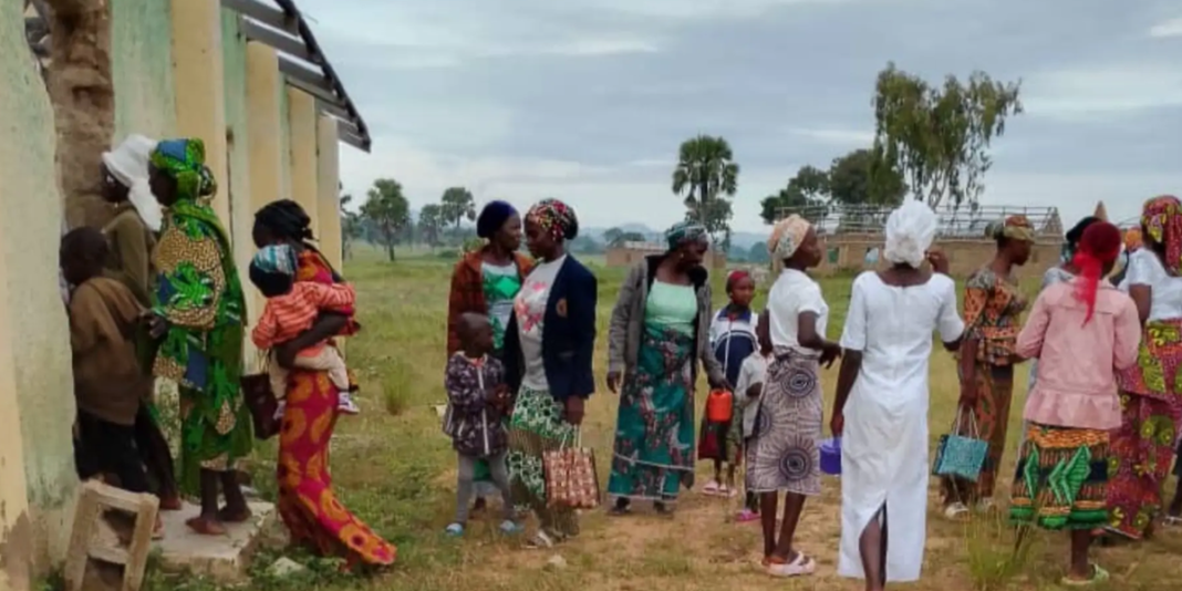 Comunidade nigeriana em estado de choque após ataque noturno, com moradores observando a destruição.