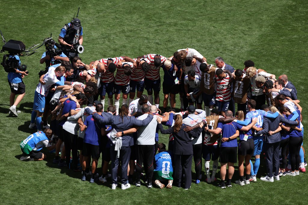 Jogadores da Seleção Masculina dos EUA ajoelhados em oração no campo após vencer a Copa do Mundo.
