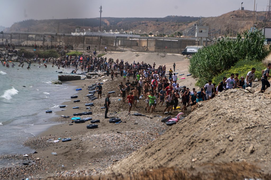 Migrantes cruzando a fronteira em direção a Ceuta, em meio a um cenário de caos e tensão.