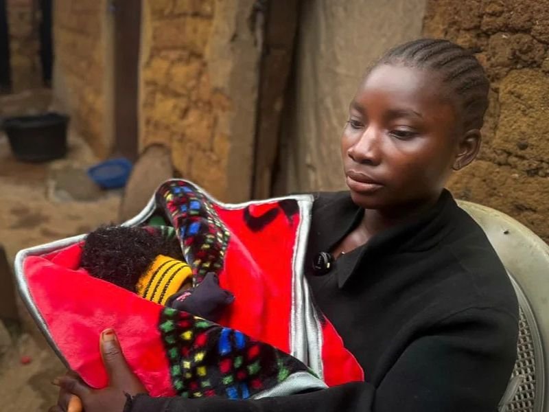 Jovem mãe nigeriana abraça seu bebê recém-nascido após sobreviver a ataque brutal.