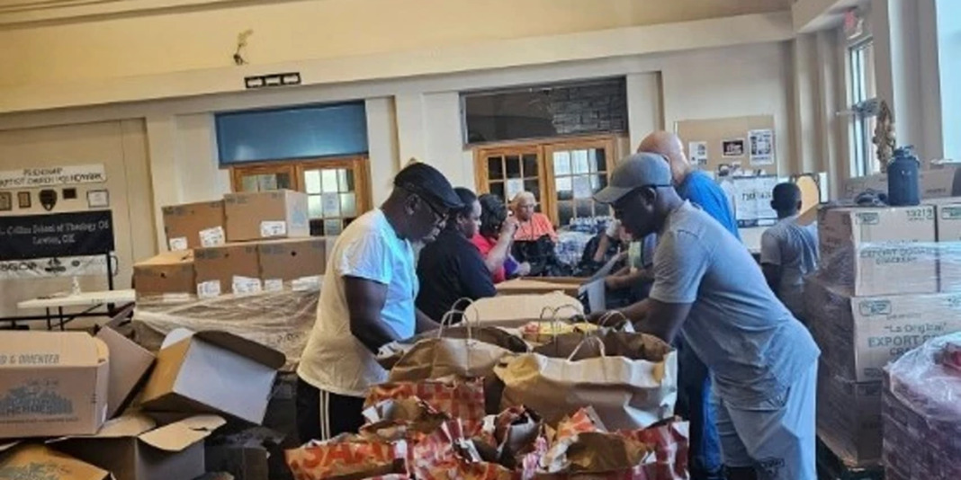 Voluntários distribuem alimentos para a comunidade em frente a uma igreja.
