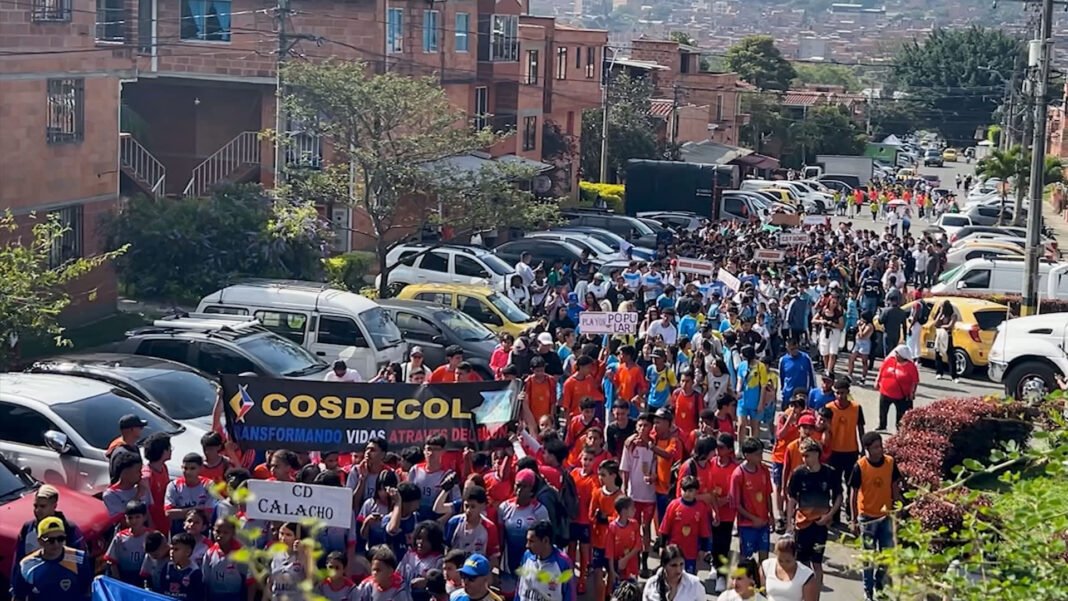 Crianças jogando futebol em um campo comunitário em Medellín, com um treinador observando.