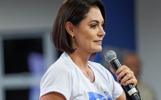 Michelle Bolsonaro em evento político sendo apoiada por aliados e público.