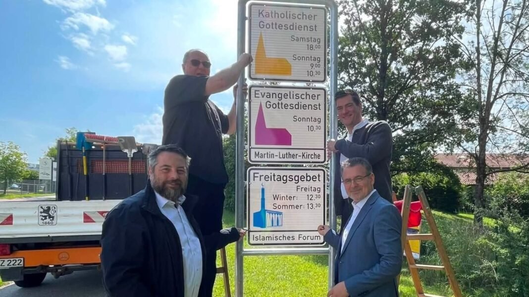 Placa oficial na entrada de Penzberg, Alemanha, mostrando horários de oração islâmica e cristã.