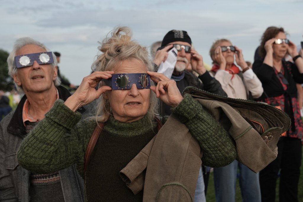 Pessoas observam eclipse solar total cobrir o sol em uma cidade europeia