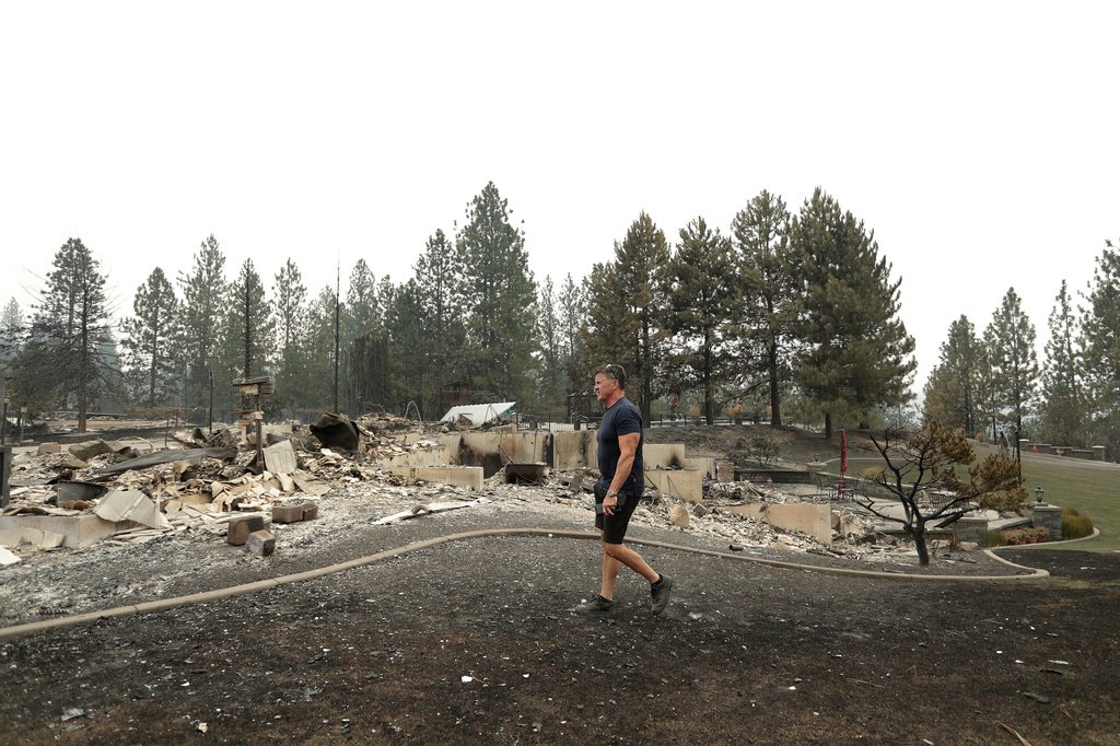Rua residencial devastada por incêndio florestal em Spokane, Washington, com casas destruídas e cinzas cobrindo o solo.