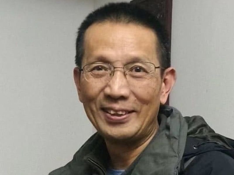 Pastor John Cao em um ambiente que remete à fronteira China-Myanmar, com expressão de esperança.